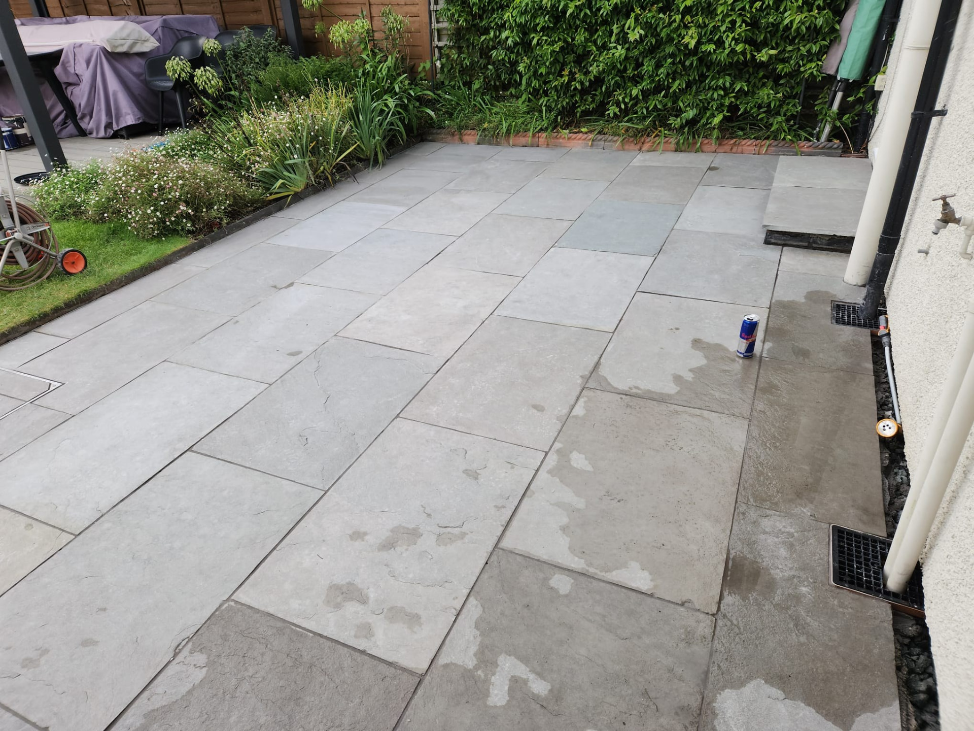 Grey sandstone patio slabs laid across a rear garden with planted border in Essex