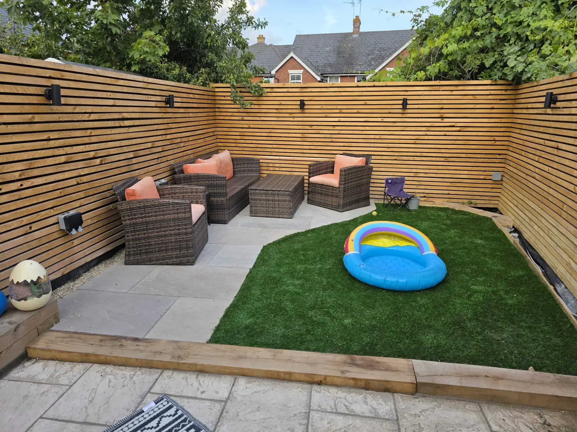 Compact Essex garden with contemporary slatted timber fencing, porcelain paving, sleeper edging and an artificial lawn